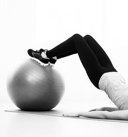 sporty woman doing pilates exercise lifting her pelvis with fit ball at home